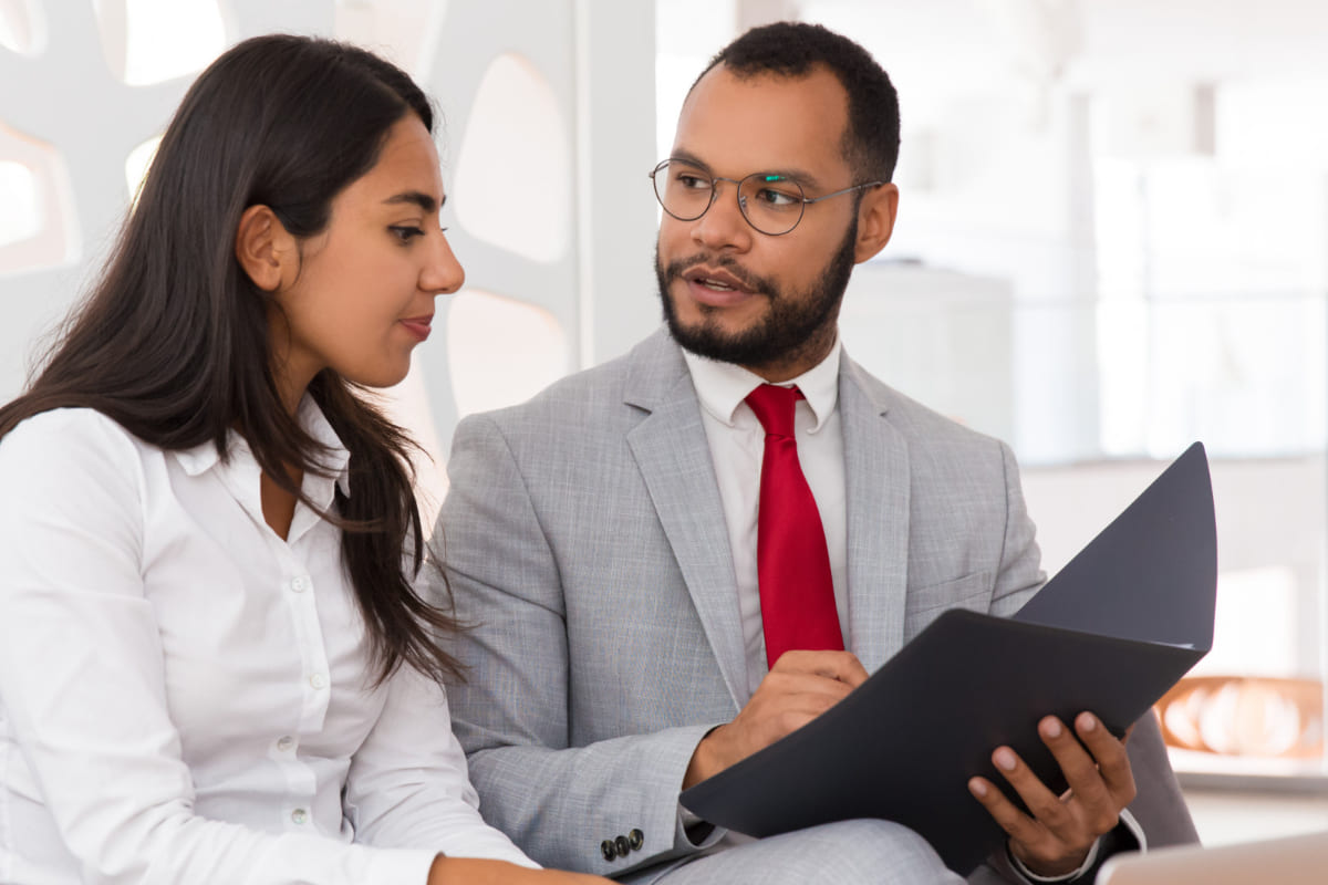 Advogado conversando com sua cliente: Marketing jurídico Marketing jurídico: A imagem mostra um advogando mostrando para uma mulher algum documento em uma pasta preta