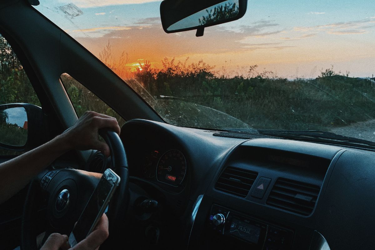 Pessoa dirigindo: Marketing no agronegócio Marketing no agronegócio: A imagem mostra uma pessoa dirigindo e fazendo o uso de um celular.