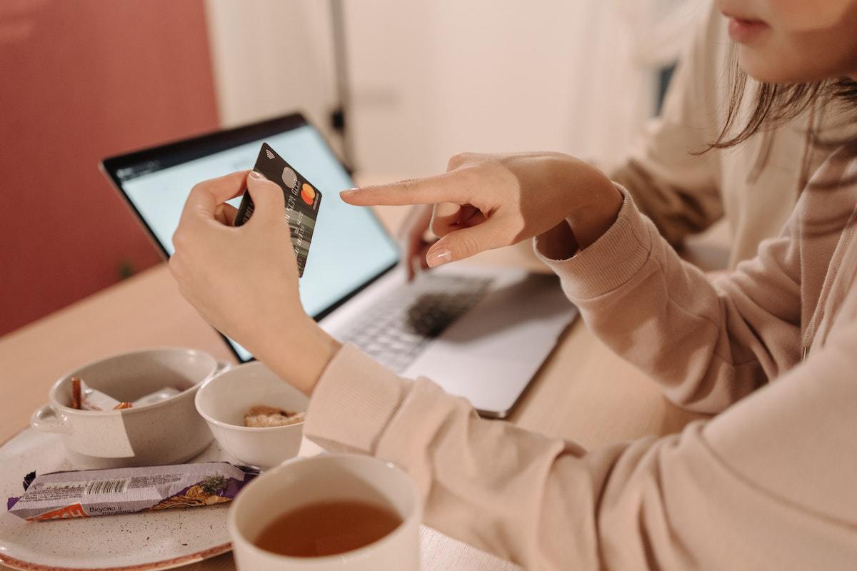 pessoa segurando um cartão de crédito enquanto usa o laptop