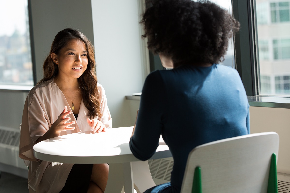 Mulheres conversando: Técnicas de venda Técnicas de venda: A imagem mostra duas mulheres conversando em uma mesa.