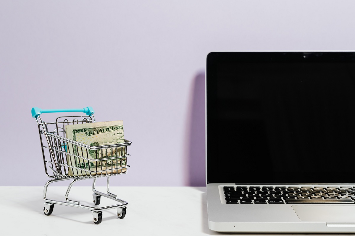 Técnicas de venda: A imagem mostra um carrinho de compras ao lado de um computador, dando a entender compras online. 