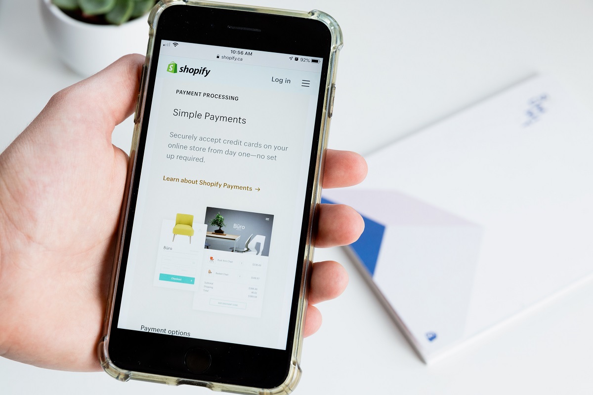 Vender um produto: A imagem mostra uma pessoa com um smartphone na mão, mostrando o site do Shopfy