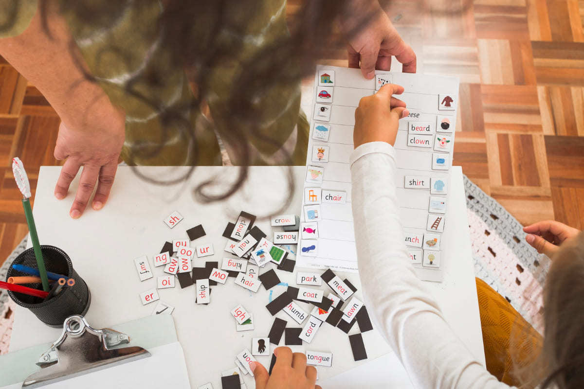 Tarefa: Abrangência do conteúdo Mulher e criança sentados no chão fazendo recortes como tarefa escolar em conjunto