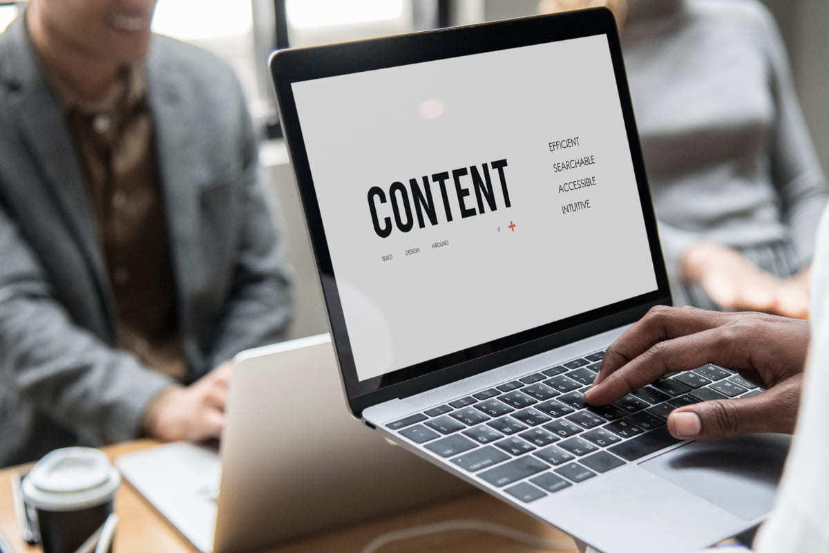 Dois homens em local de trabalho usando notebooks onde um deles apresenta em sua tela uma montagem com o nome content