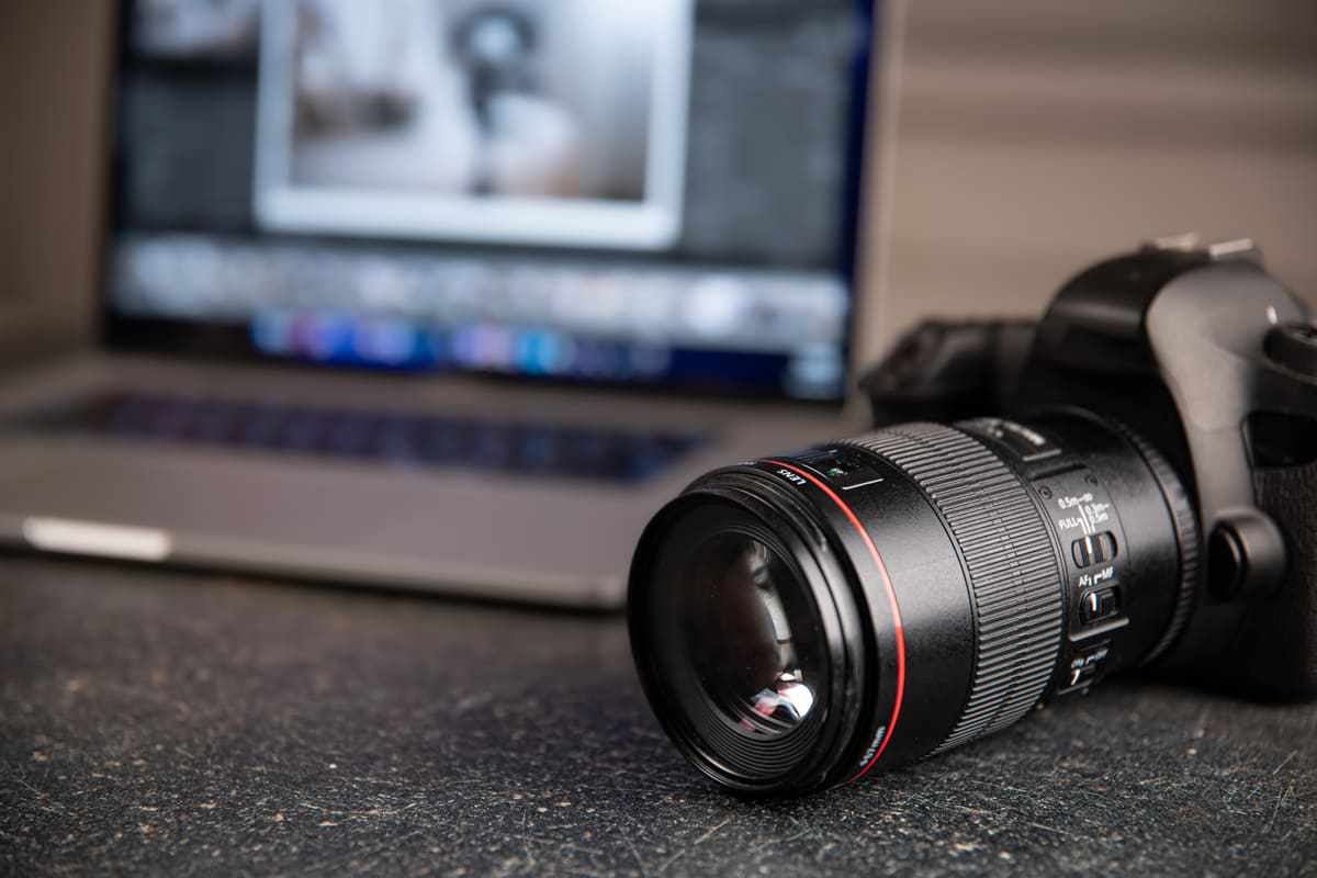 Câmera: Adobe Lightroom Câmera fotográfica sobre superfície preta e notebook ao fundo