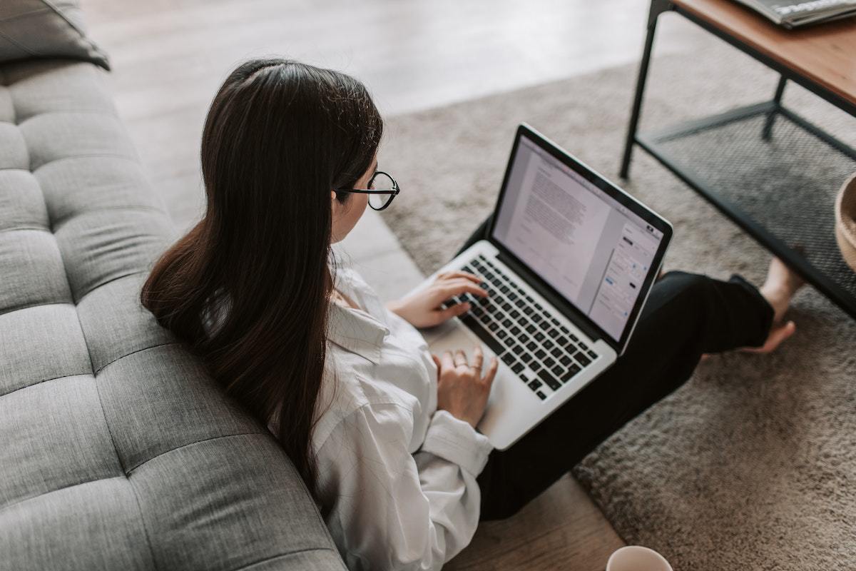 Mulher sentada no chão sobre tapete felpudo na frente de mesa de centro com notebook no colo conferindo conteúdo no Alexa ranking para estratégia de marketing