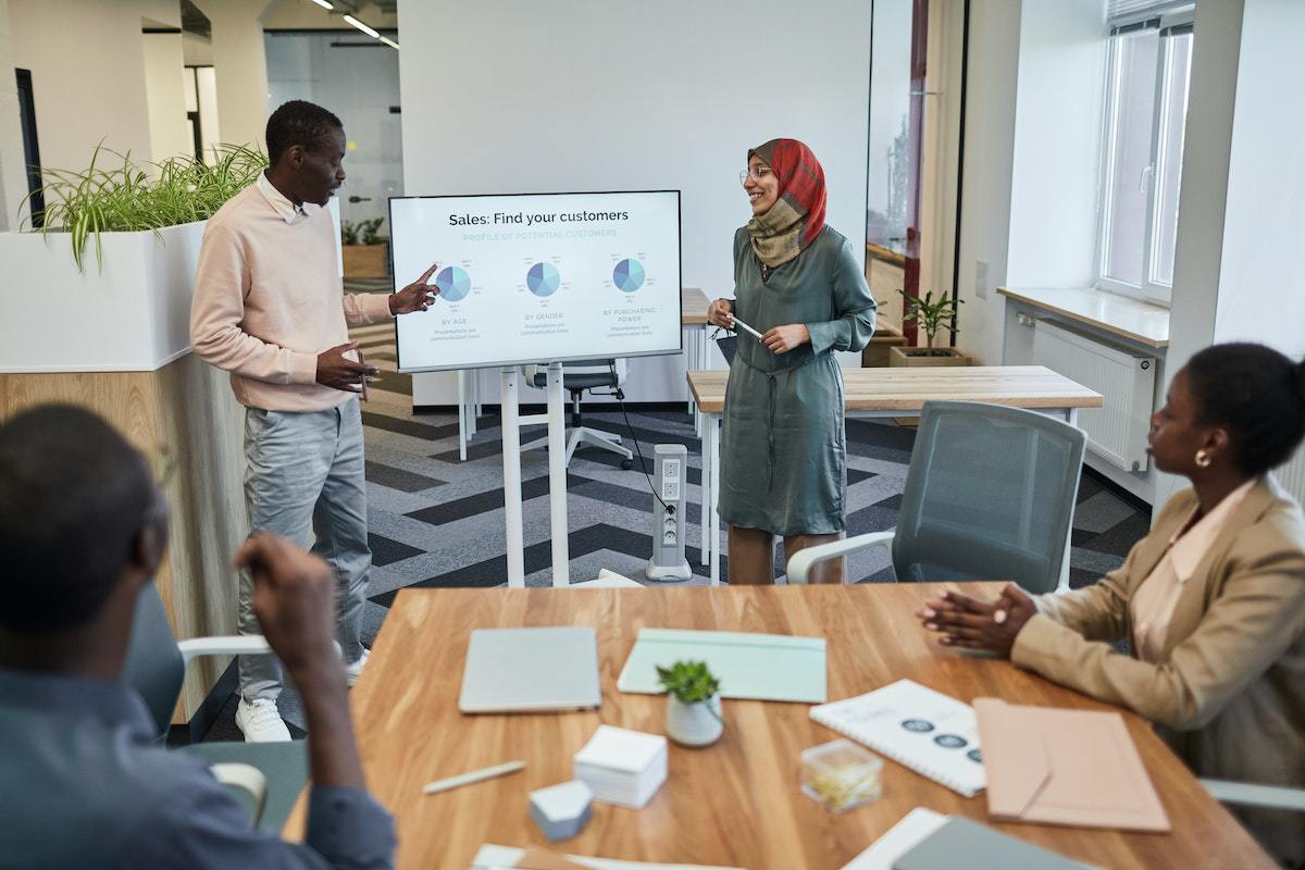 Homem e mulher liderando reunião e fazendo Apresentação no powerpoint diante de outros colegas em empresa inclusiva