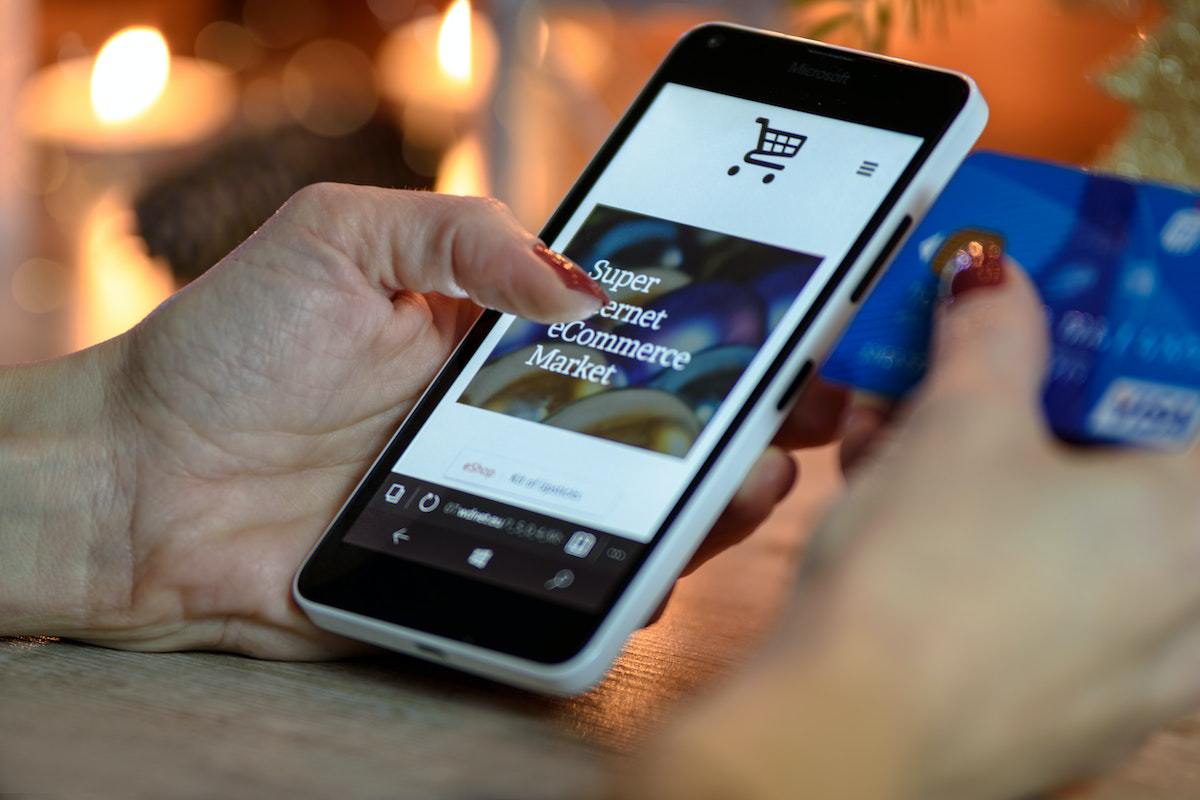 Mulher segurando celular e cartão de crédito enquanto faz compra online