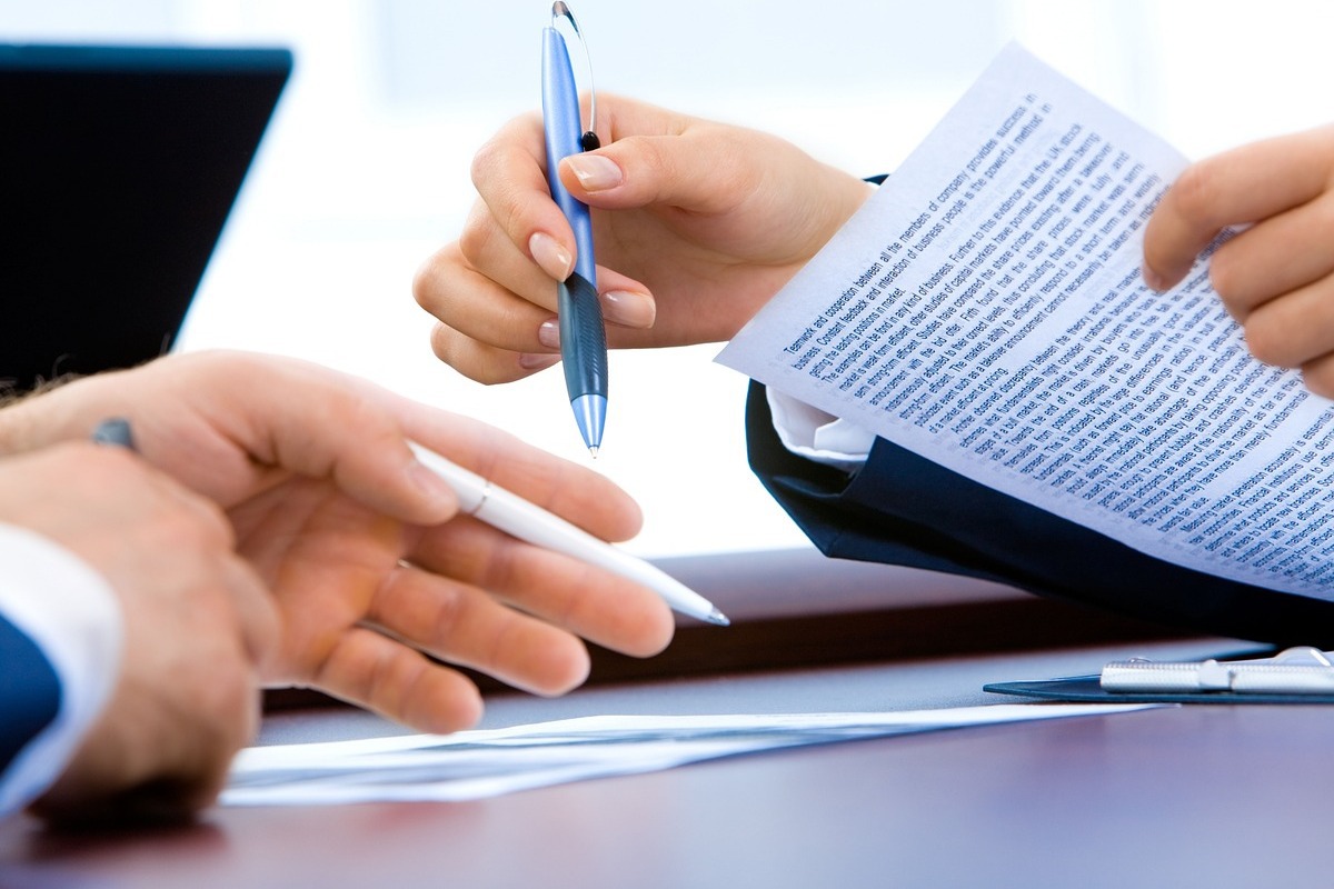 Escritório: BV Mãos de duas pessoas diferentes onde cada uma segura uma caneta de cor diferente enquanto analisam papéis que parecem contrato sobre mesa em escritório