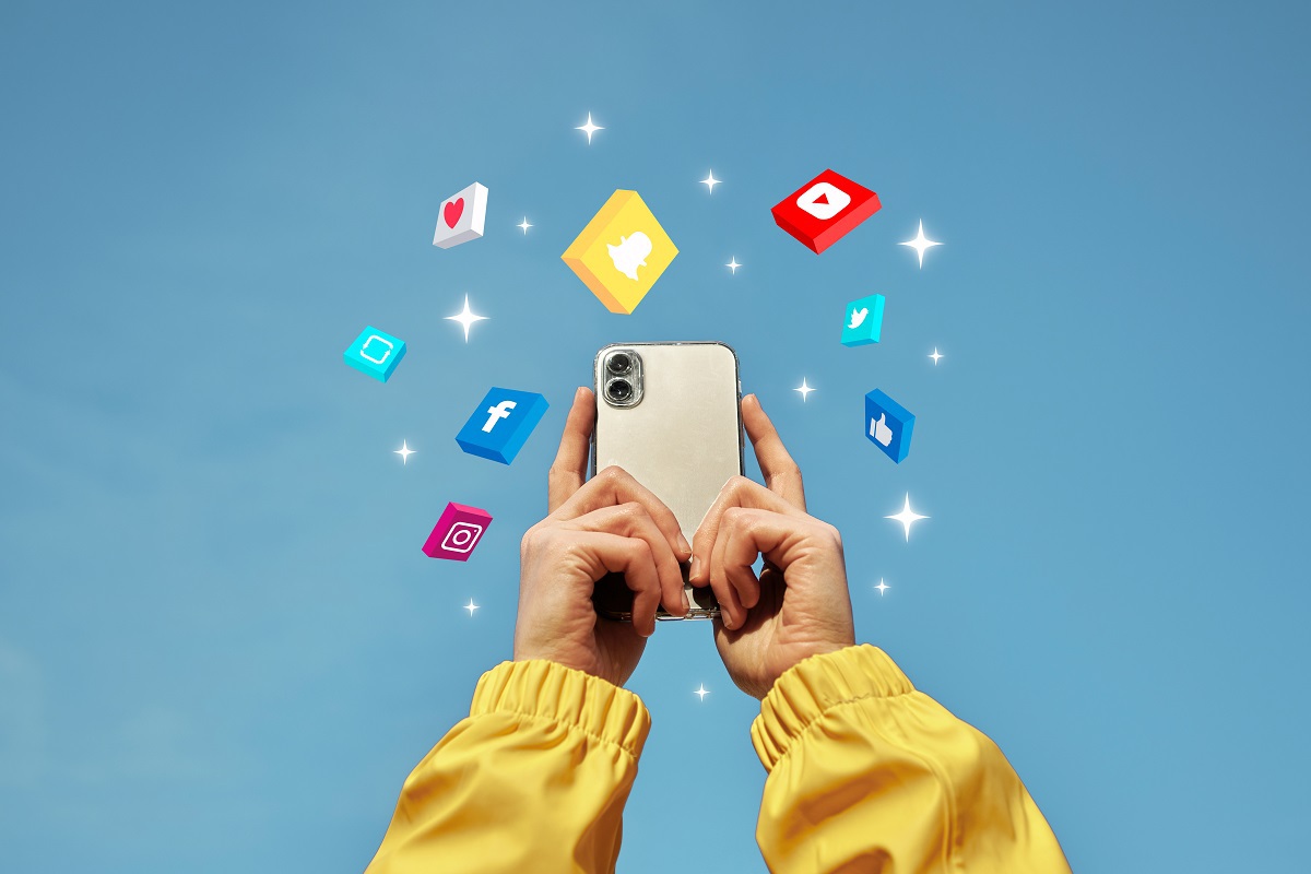 Pessoa segurando smartphone enquanto ergue o mesmo e sinais de redes sociais saindo do mesmo em montagem de foto com fundo azul