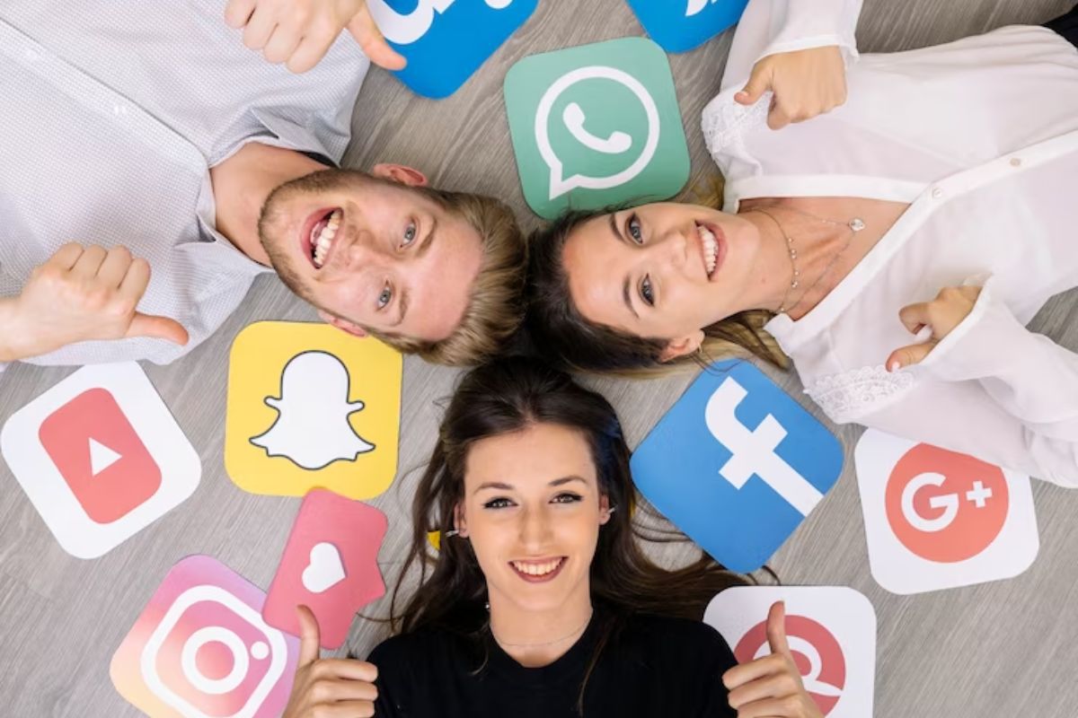Pessoas deitadas no chão com símbolos de redes sociais impressos ao redor dos mesmos, que sorriem para foto