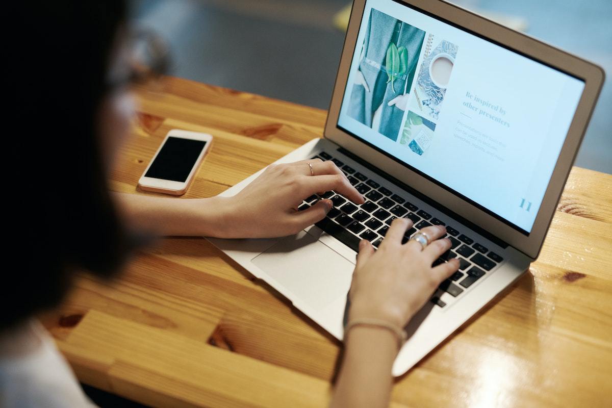 Mulher usando notebook sobre mesa de madeira ao lado de smartphone usando Blog pessoal em home office
