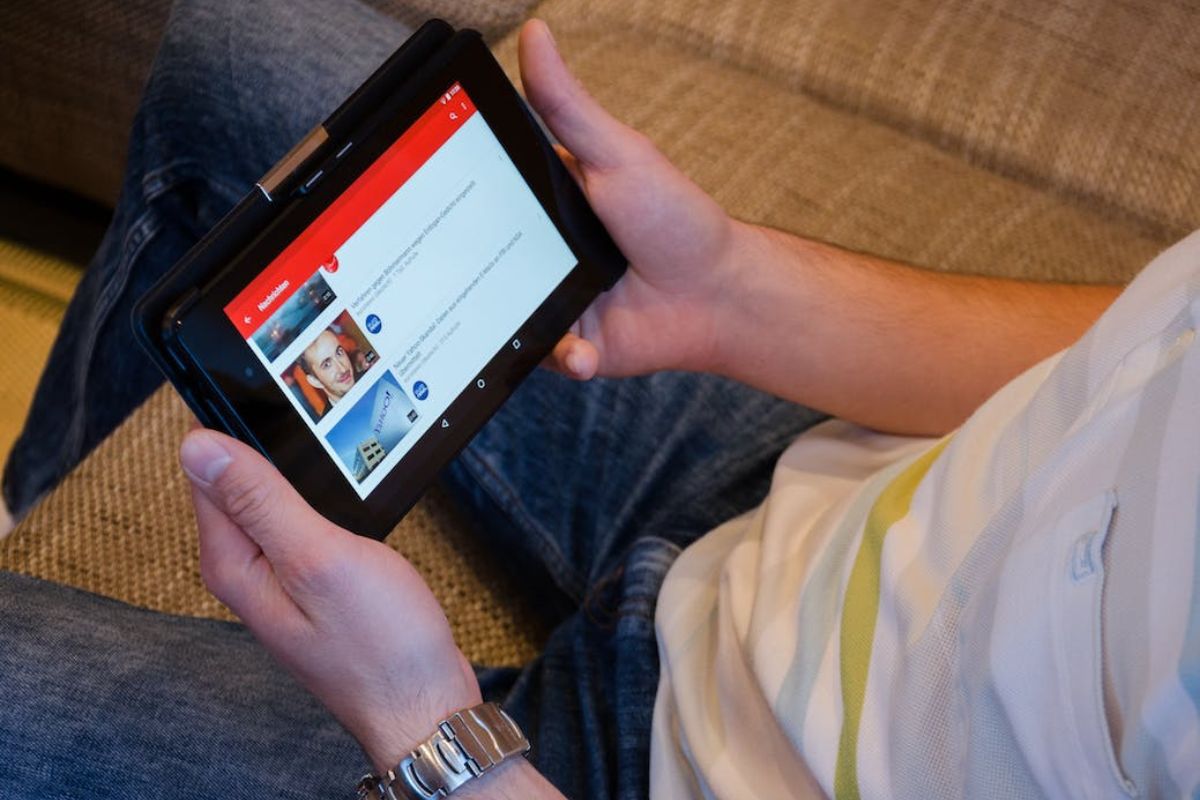 Homem sentado em sofá segurando tablet e procurando vídeos no YouTube