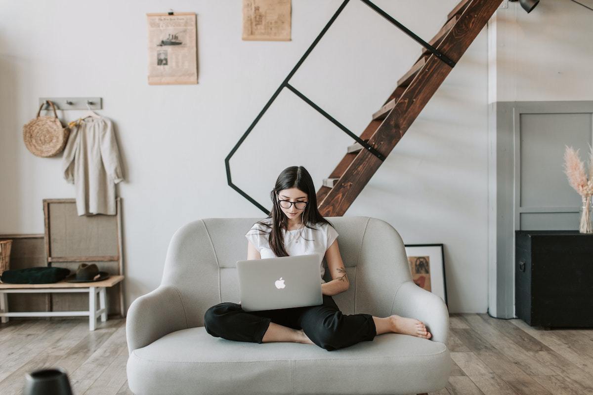 Mulher sentada em sofá com notebook no colo trabalhando em home office com Dropshipping com decoração nas paredes ao seu redor