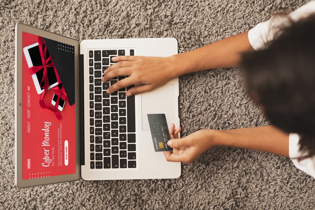 Notebook: Estratégia multicanal Pessoa usando notebook sobre tapete felpudo no chão segurando cartão de crédito em compra online