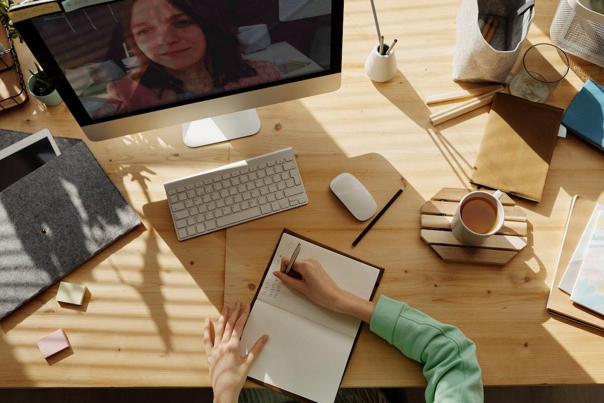Mulher sentada diante de mesa de madeira em reunião online com outra mulher na tela em recurso que ajuda na Evolução marketing educacional