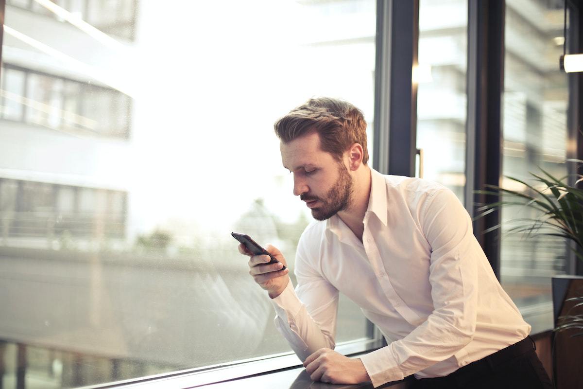 Homem em fintech sentado diante de janela de vidro usando smartphone concentrado
