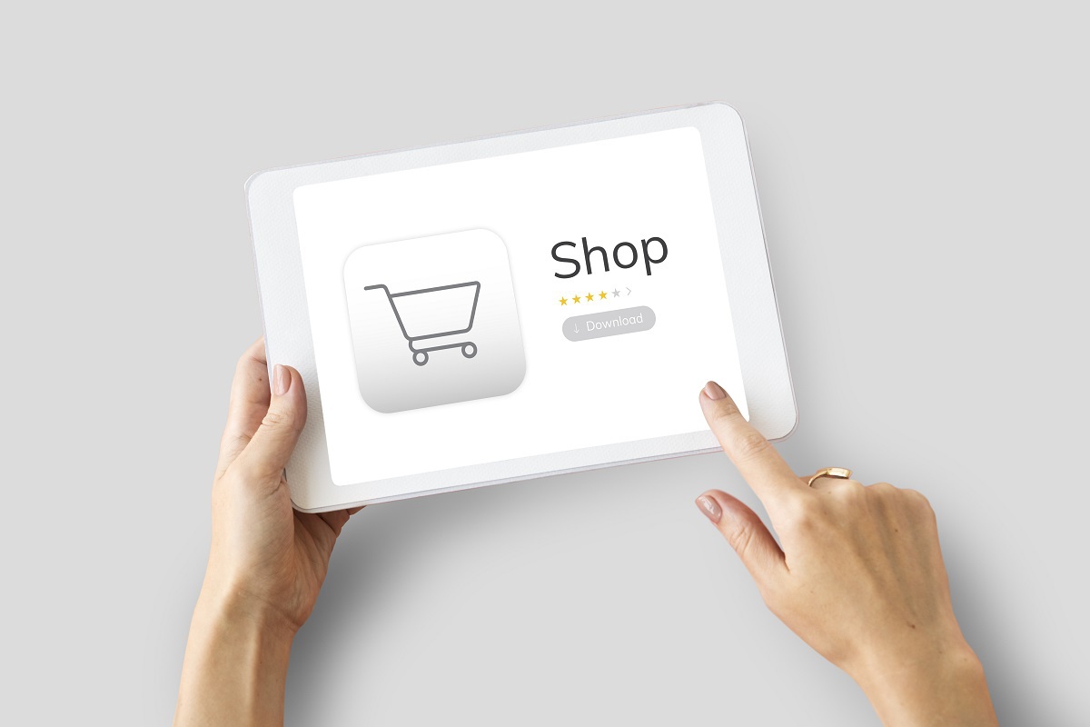 Mulher segurando tablet branco com montagem escrita Shop e carrinho de compras representado por símbolo web de carrinho de compras