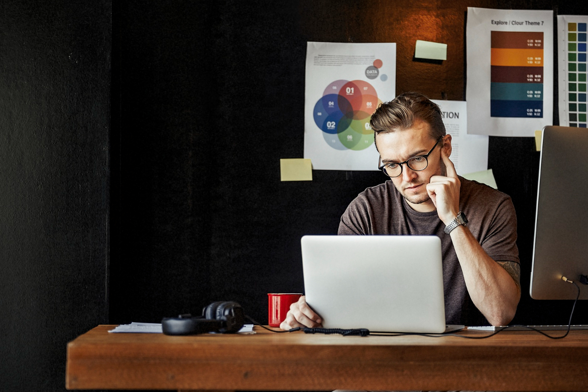 Notebook: Freelancer de marketing digital Homem trabalhando em notebook sobre mesa de madeira com decoração ao fundo e objetos de escritório ao seu redor