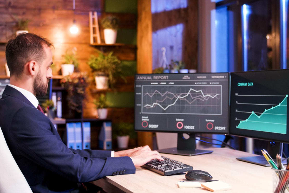 Homem analisando gráficos em computador sobre mesa de madeira usando terno em empresa