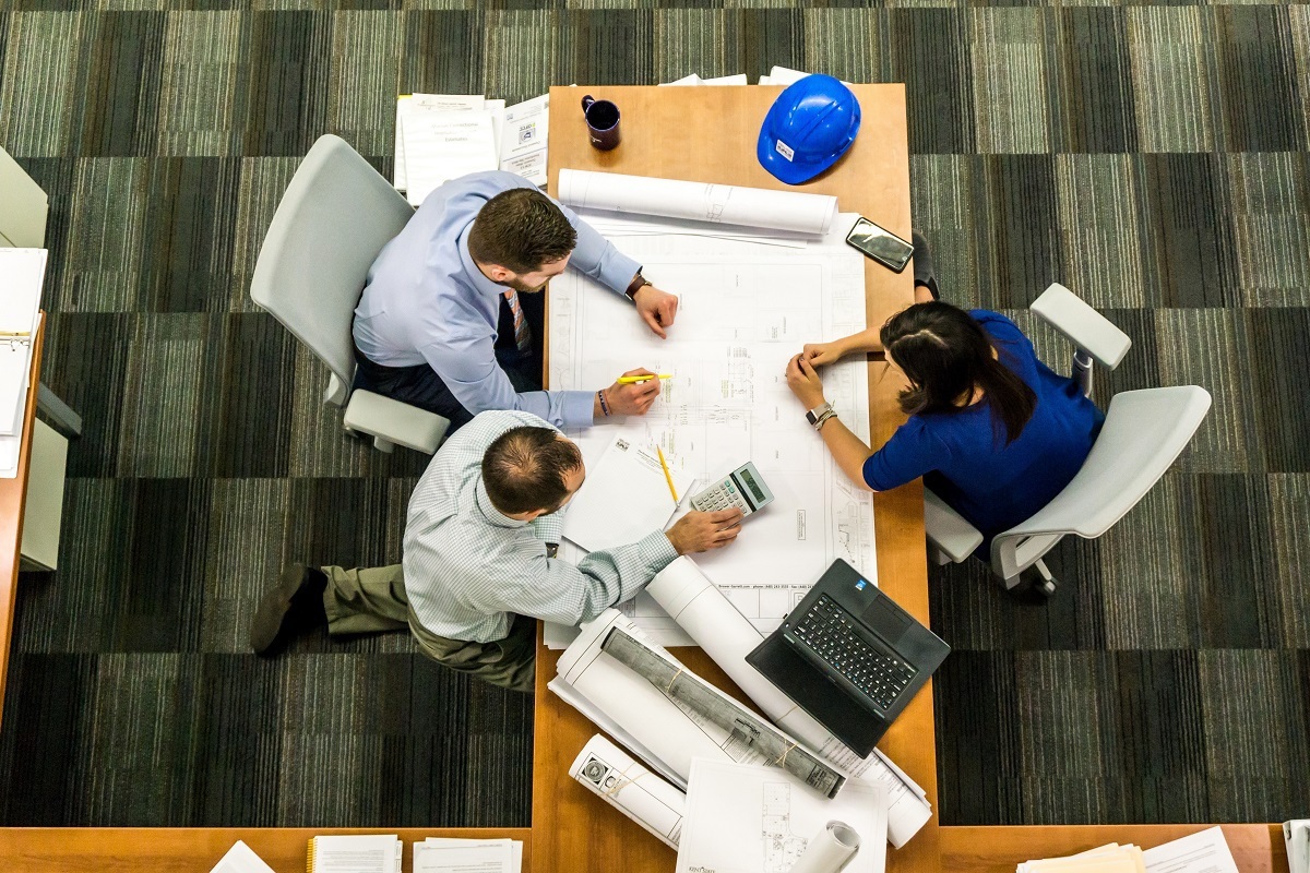 Escritório: Gestão integrada Mulher diante de mesa de madeira com dois homens sentados ao outro lado em escritório