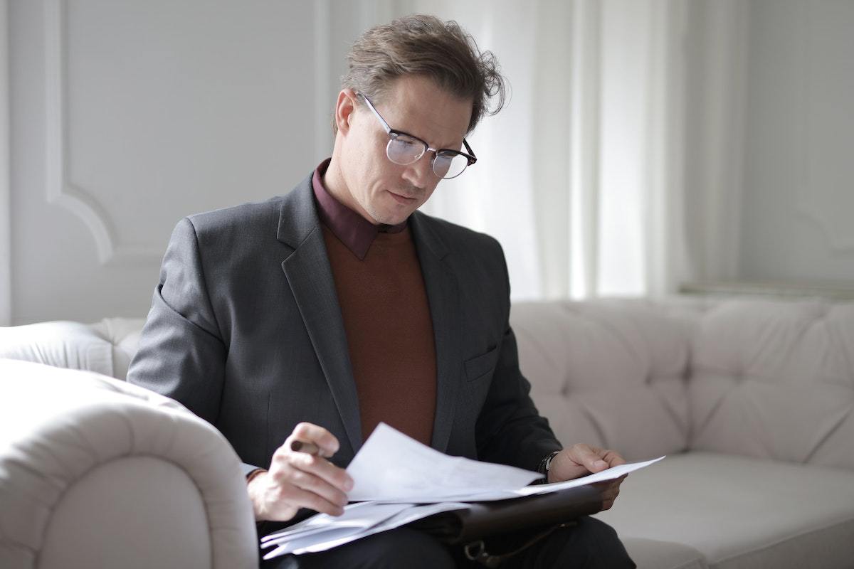 Gestor de empresa sentado em sofá analisando dados em folhas a4
