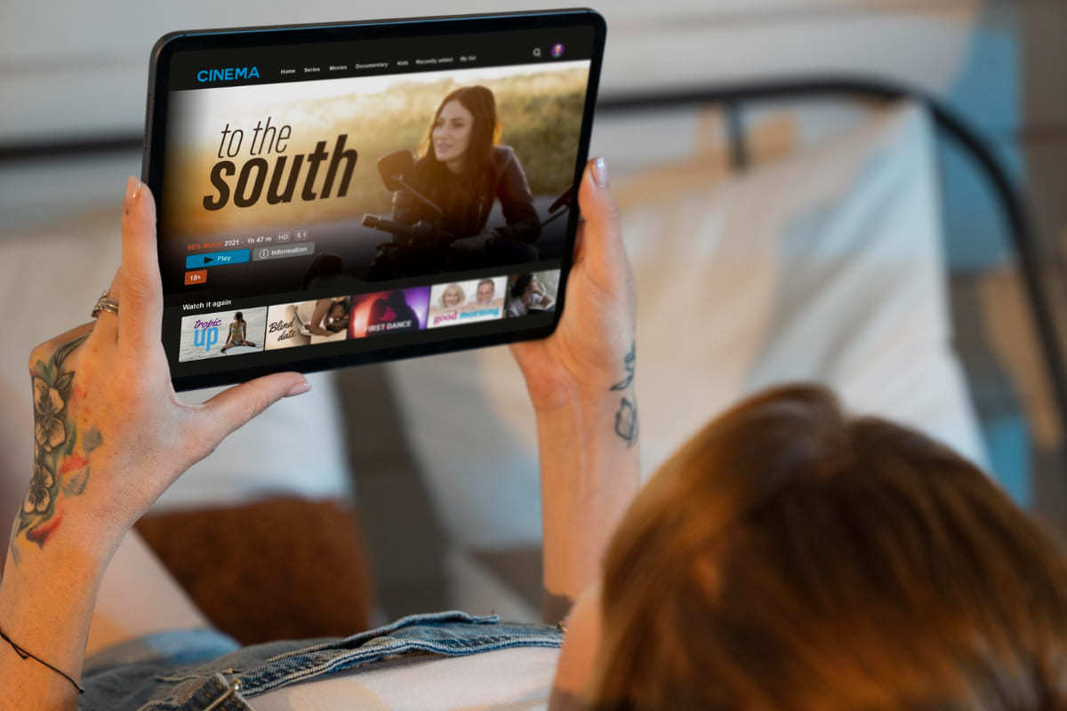 Mulher com tablet preto na mão enquanto assiste série no mesmo e com propagandas na parte inferior da tela
