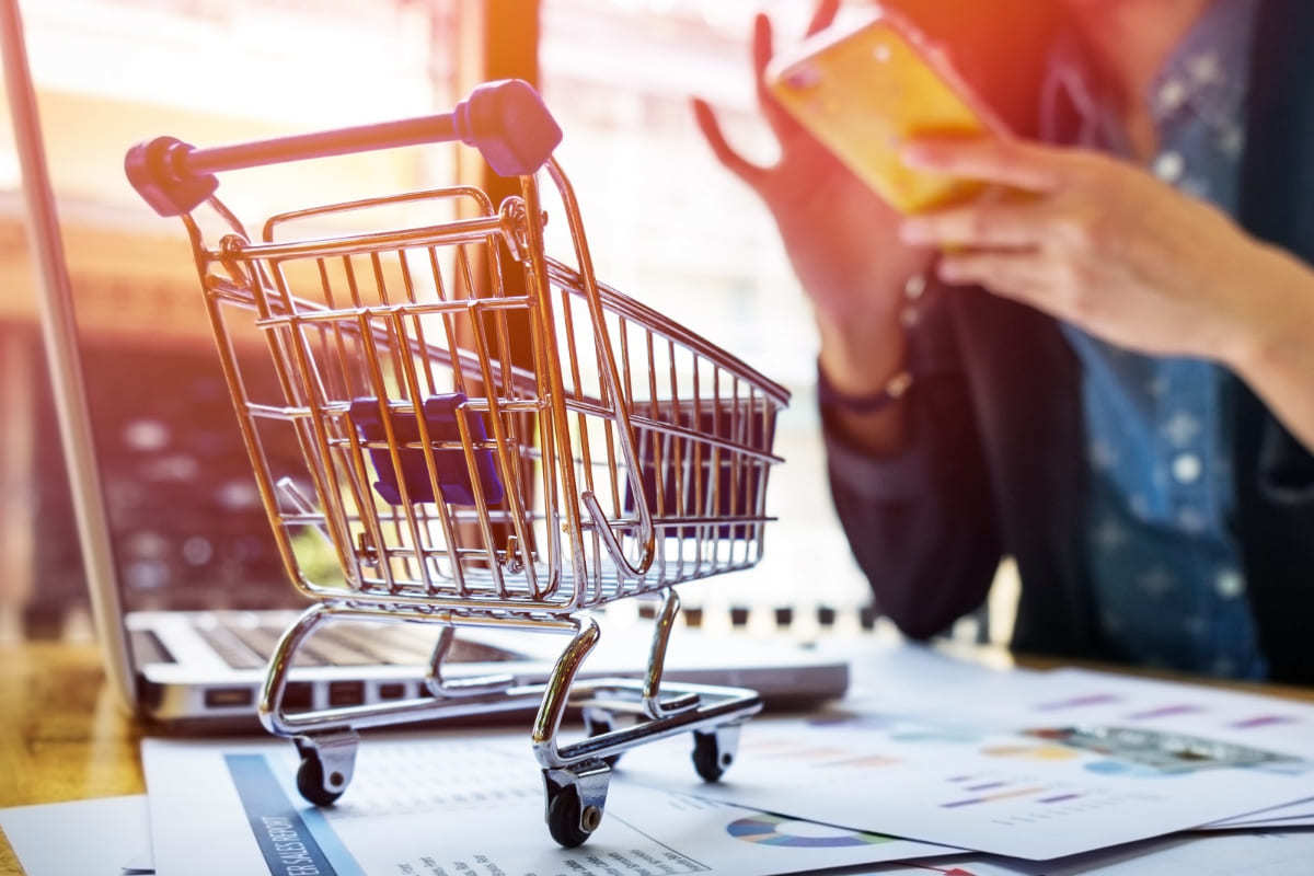 Dados: Hacking sales Pessoa com celular nas mãos usando técnicas de Hacking sales com dados impressos em sua frente sobre mesa além de carrinho de compras pequenas sobre as mesmas em montagem gráfica para representar o tema