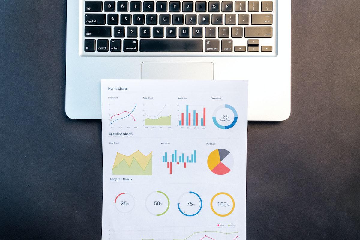 Gráficos impressos em folha sobre teclado de notebook cinza em cima de mesa preta