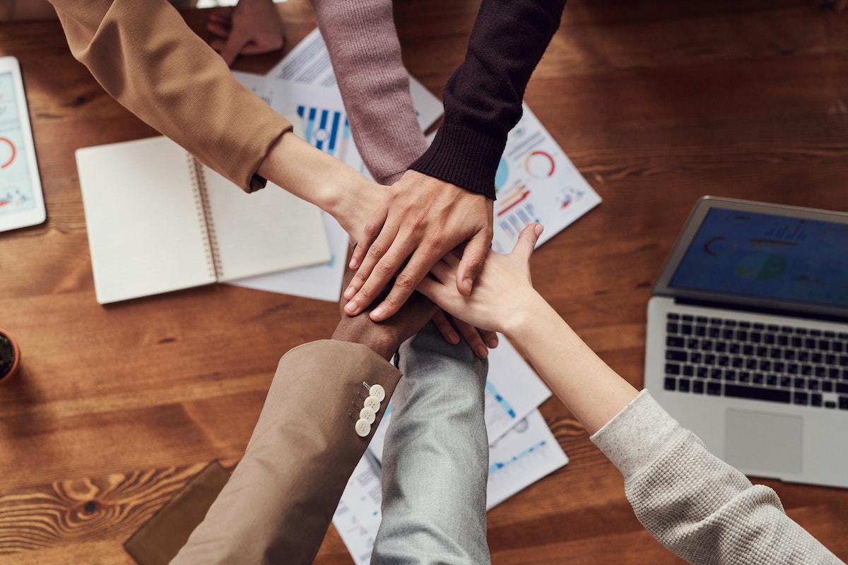 Time composto para Lançamento afiliado se cumprimentando dando as mãos em reunião de trabalho com dados impressos em folha de papel sobre mesa de madeira e ao lado do notebook