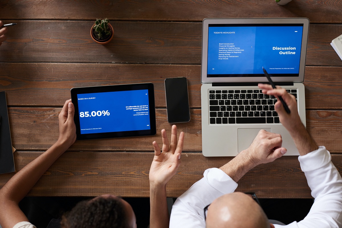 Dados: Lançamento semente Duas pessoas sentadas diante de mesa de madeira analisando dados em tablet e notebook com celular preto entre eles