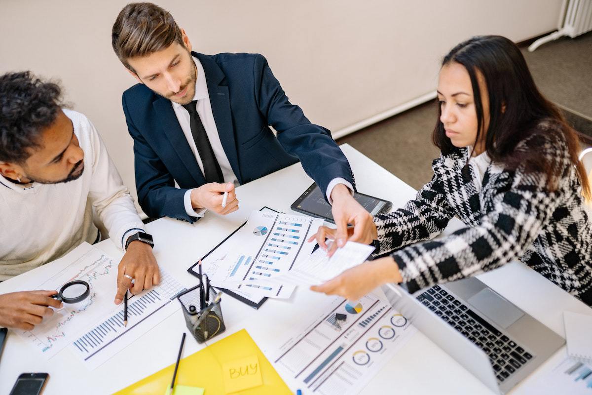 Dois homens e uma mulher em reunião de trabalho analisando dados em folhas impressas
