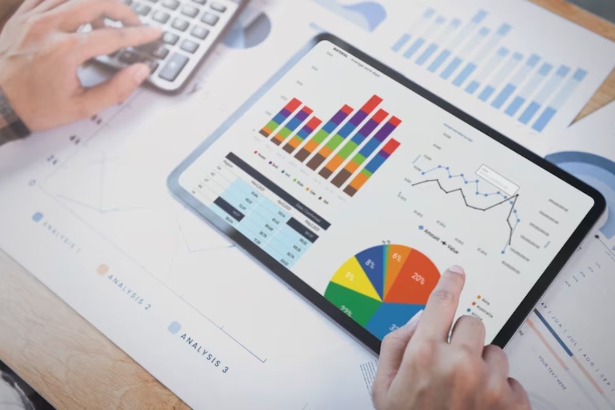 Homem analisando Métricas de vídeo em tablet e folhas de papel a4 impressas, enquanto usa calculadora com mão esquerda