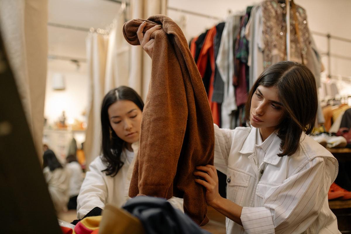 Duas mulheres usando computador em cima de balcão de local análogo à loja de roupas como forma de People marketing
