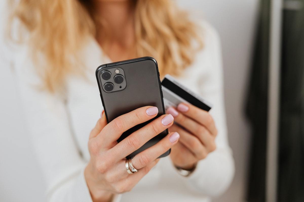Mulher segurando celular e cartão de crédito enquanto faz compra online