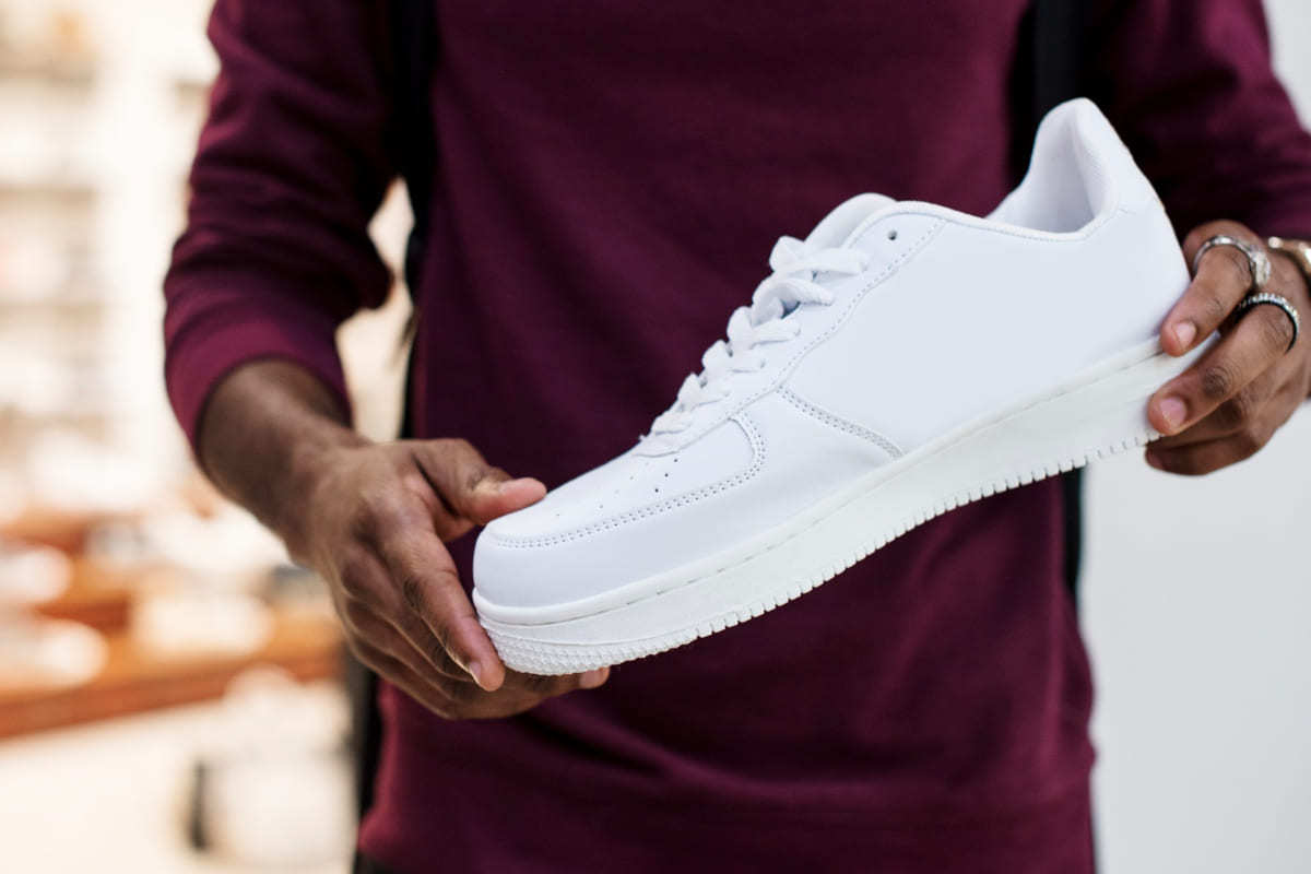 Loja: Pop-up store Homem segurando tênis branco enquanto aparentemente o analisa com propósito de comprá-lo em loja Pop-up store