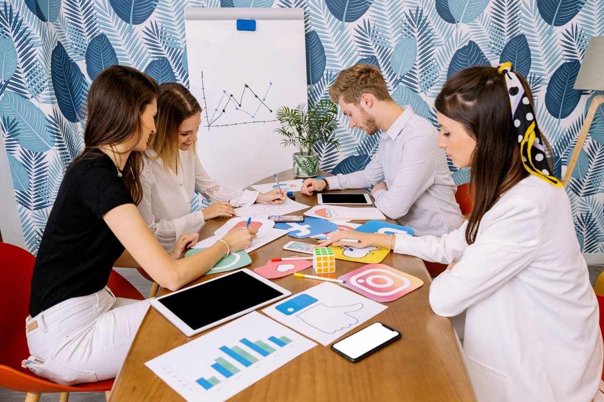Equipe reunida em local de trabalho decidindo Posicionamento de mercado com gráficos e símbolos de redes sociais e analisando dados em tablets e notebooks