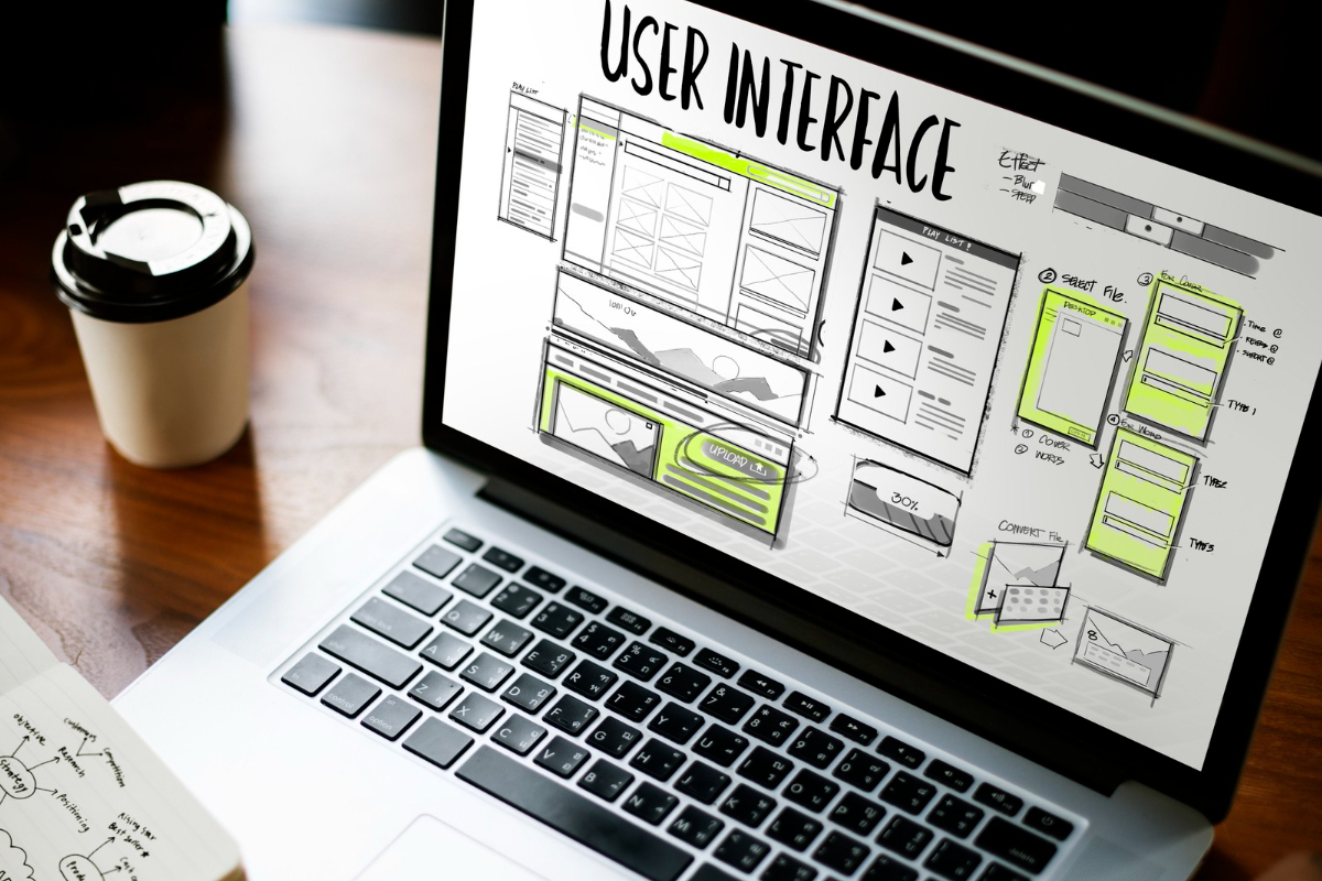Projeto: Práticas de usabilidade do site Notebook com desenho de interface do usuário em processo de melhoramento sobre mesa de madeira e ao lado de copo de café