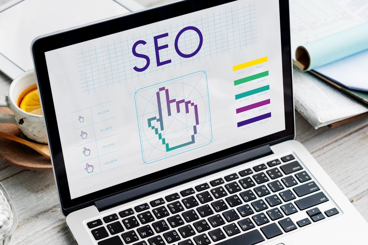 Notebook: SEO Split test Notebook sobre mesa ao lado de itens de escritório e xícara de café com montagem com sigla SEO em sua tela