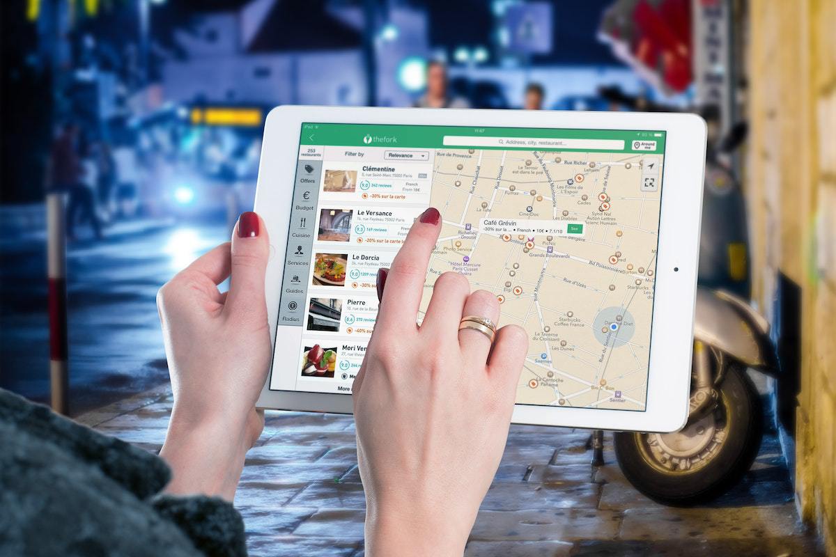 Tablet: SEO local para grandes empresas Mulher usando tablet na rua e analisando endereço em mapa