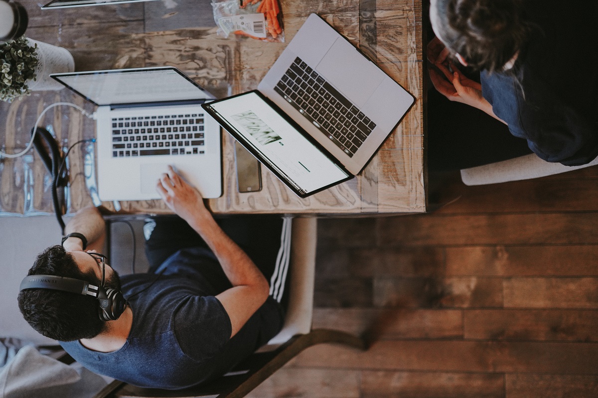 Pessoas em local de trabalho ao redor de mesa de madeira usando notebooks
