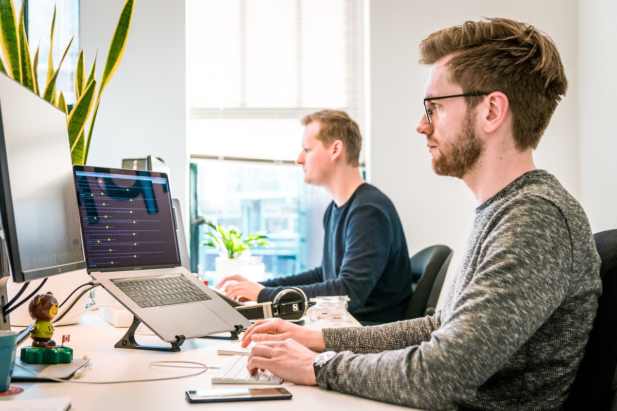 Dois homens trabalhando lado a lado em escritório usando notebooks como Sales analyst