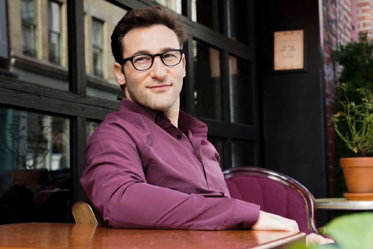 Simon Sinek sentado em local com mesa de madeira