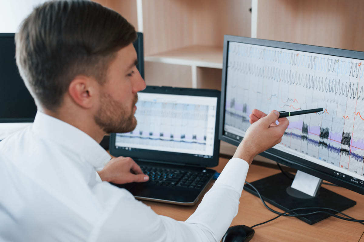 Dados: SugarCRM Homem analisando dados em monitor grande acoplado à notebook sobre mesa de madeira