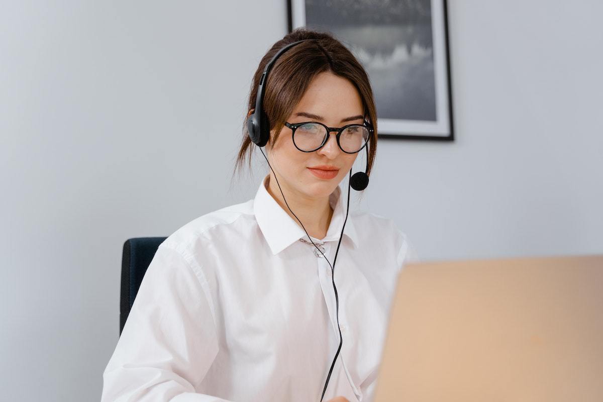 Mulher de branco sentada diante de notebook com fone de ouvido em atendimento