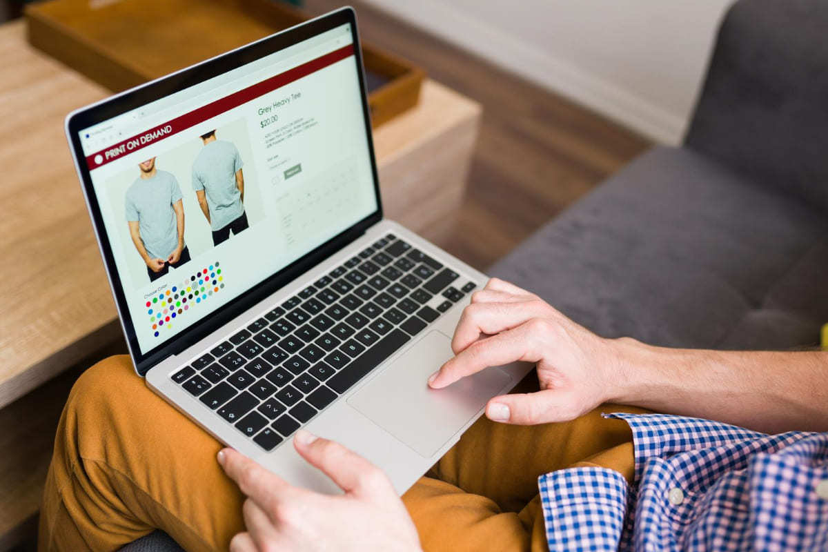 Loja online: Teste A/B para e-commerce Homem sentado em sofá usando notebook em loja online escolhendo camisa em site