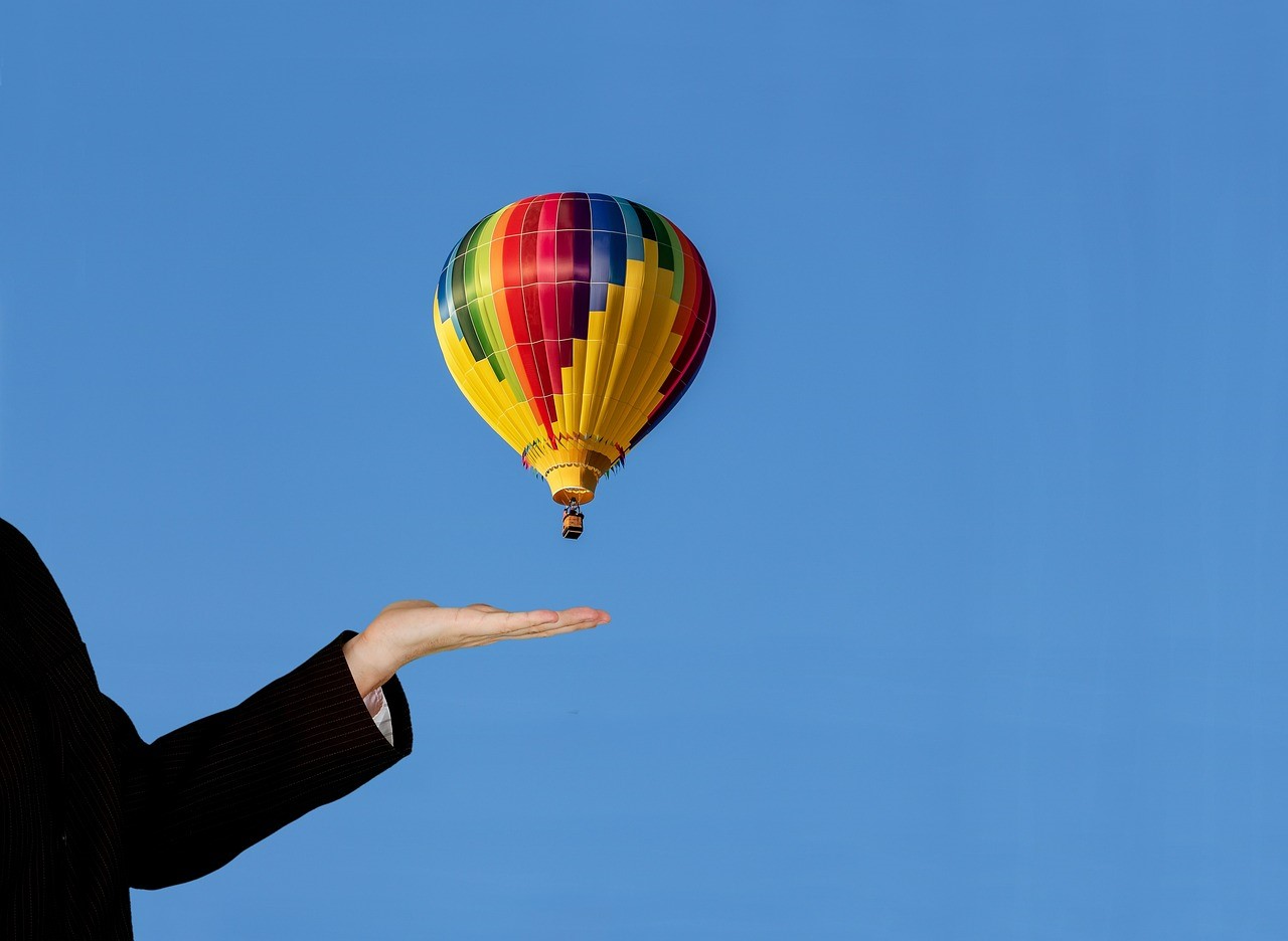 Pessoa com braço esticado e mão erguida mostrando balão do céu em fotografia