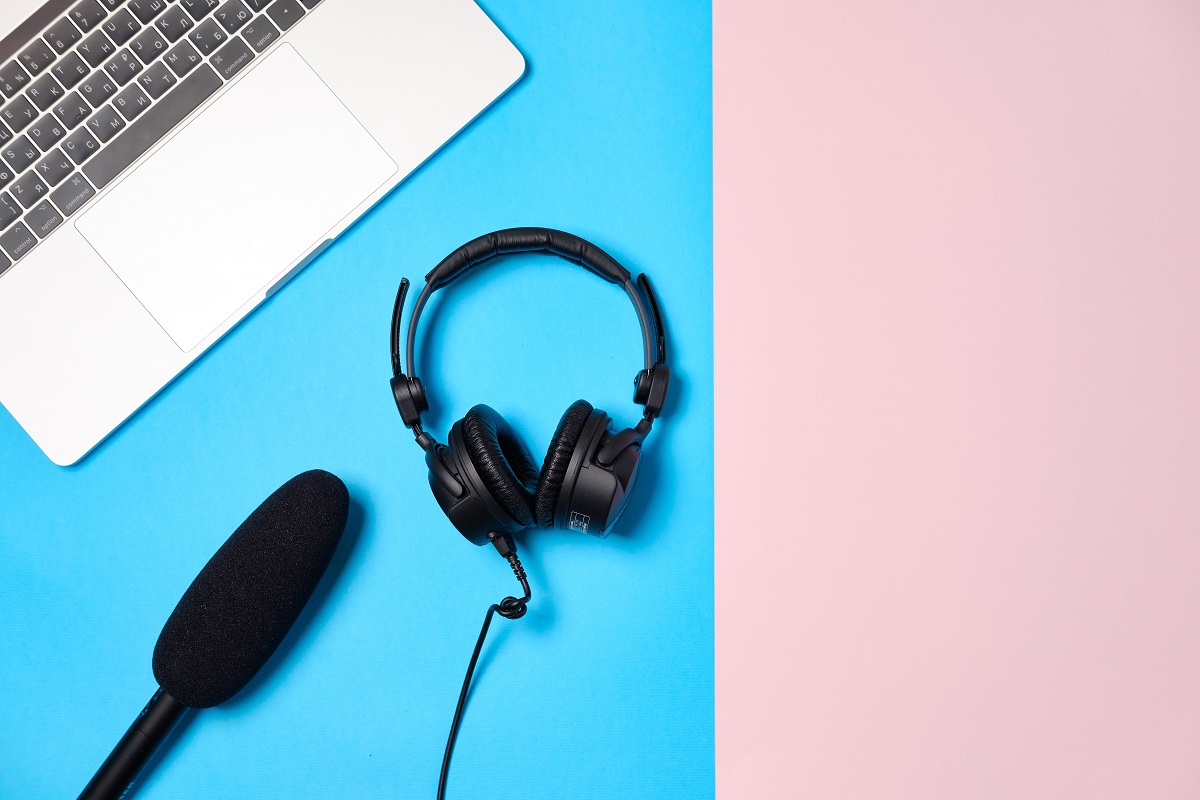 Fone de ouvido, microfone e notebook sobre superfície azul e rosa em montagem