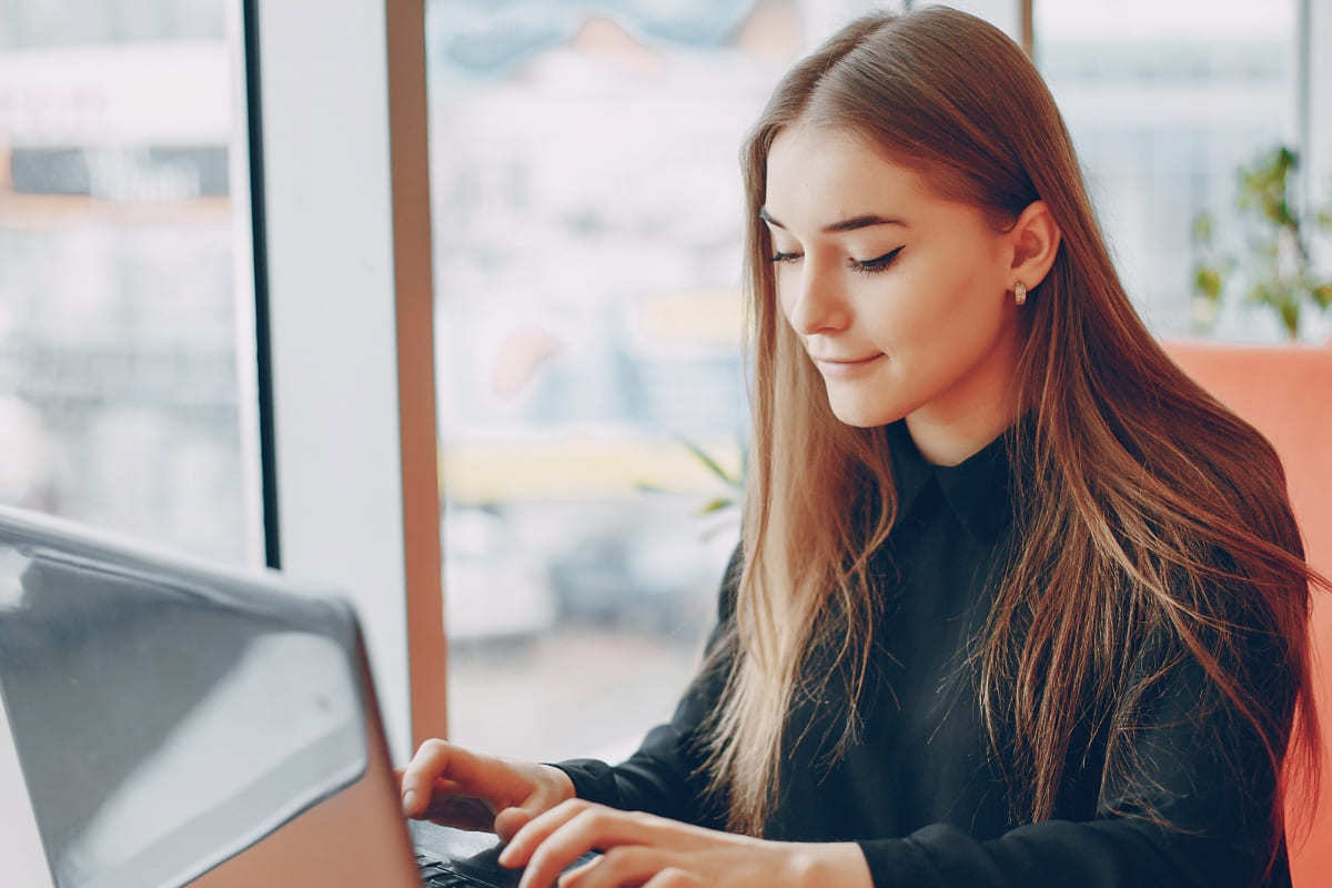 Mulher trabalhando em escritório usando Twitter analytics diante de janela de vidro em edifício com notebook