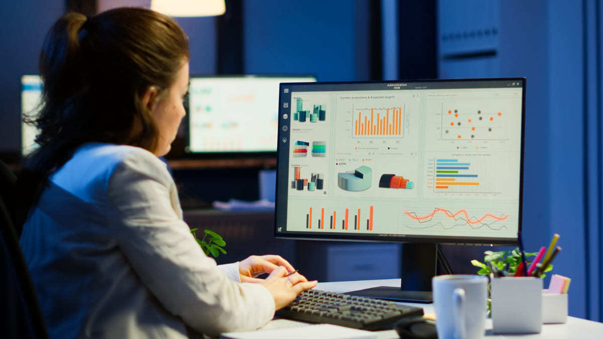 Computador: Twitter analytics Mulher trabalhando em computador com monitor preto analisando gráficos com outros monitores ao fundo em desfoco